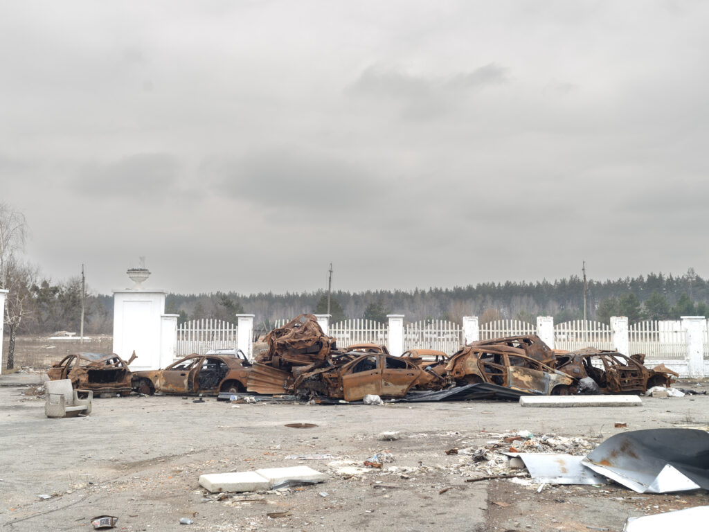 Des dizaines de véhicules détruits forment un long amas rouillé dans un espace ouvert sous un ciel gris.