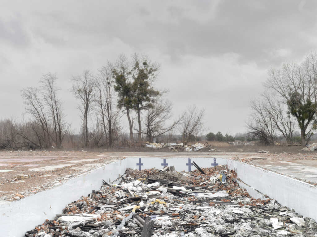 Un tas de débris occupe le centre d'une allée bordée de dalles et de petites croix, parmi des arbres dépouillés.