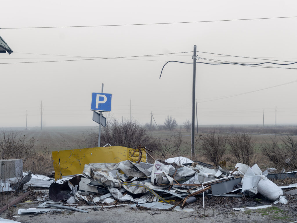 Un amas de tôles et de matériaux métalliques est déposé au pied d'un panneau de stationnement, dans un paysage ouvert.